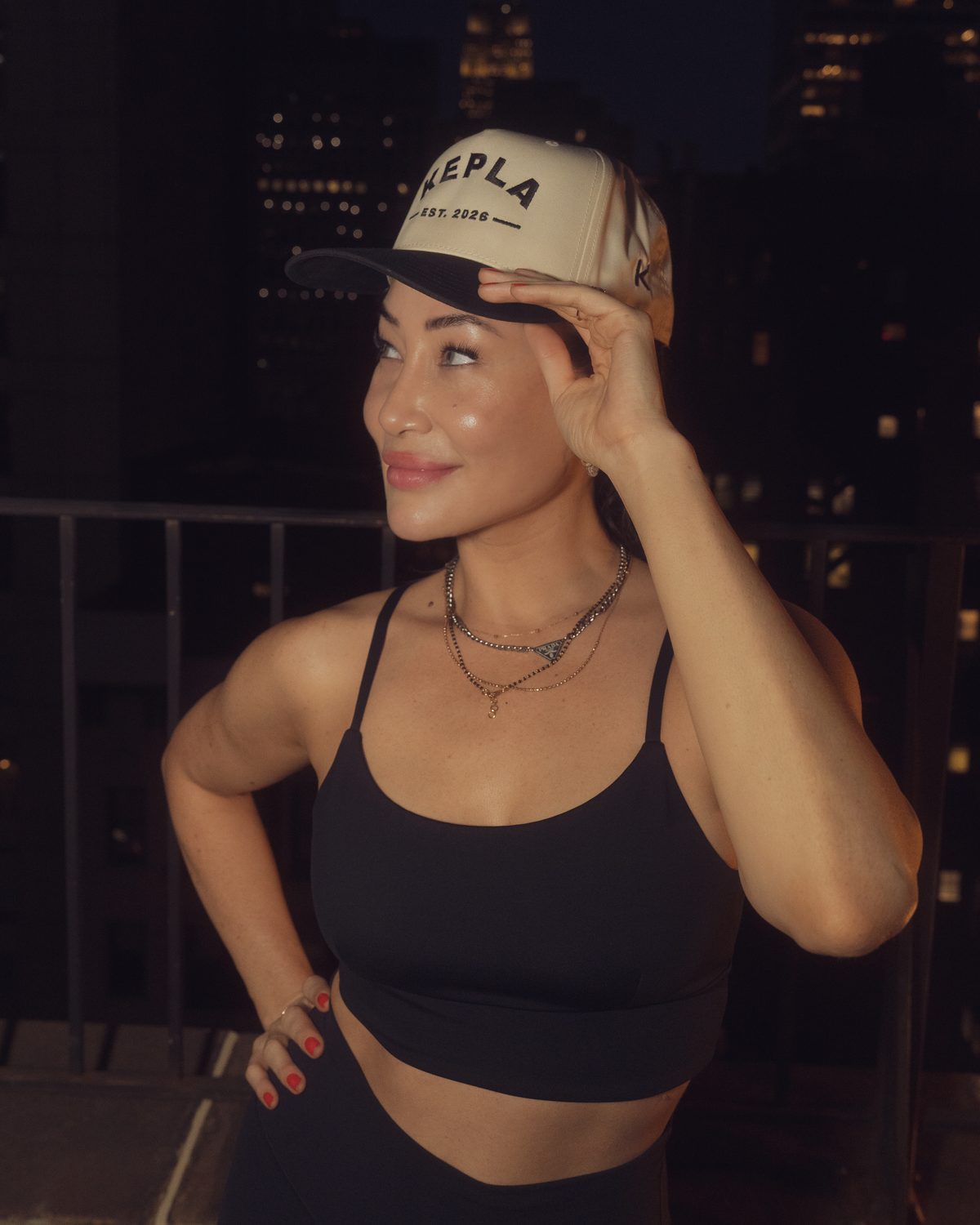Model in the Kepla hat, natural crown and black brim with KEPLA EST. 2026 embroidery, New York skyline at night